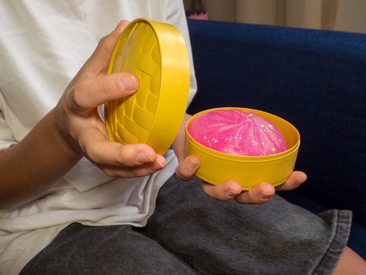 Close-up of hands unboxing a pink glittery squishy from a steamer basket